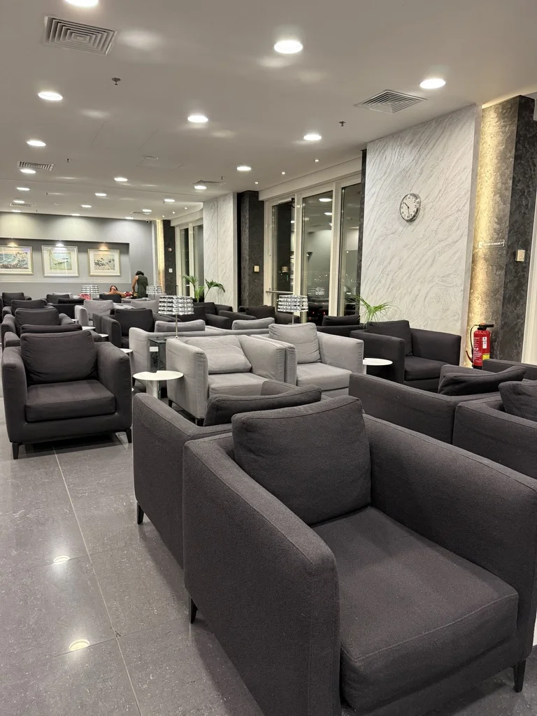 Rows of grey armchairs, sofas and small white tables in the quiet Goldair Handling Intra Lounge at Athens Airport